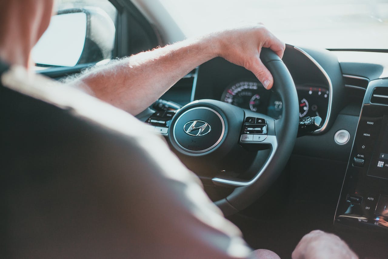 About A close-up view of a person's hand gripping a Hyundai steering wheel inside a car.
